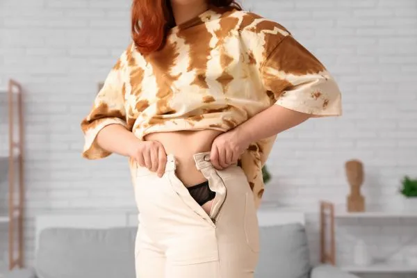 Image of woman trying to do her trousers up after pregnancy weight gain Beaconsfield